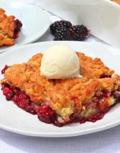 Slice of blackberry cobbler with a mound of vanilla ice cream on top, served on a white plate