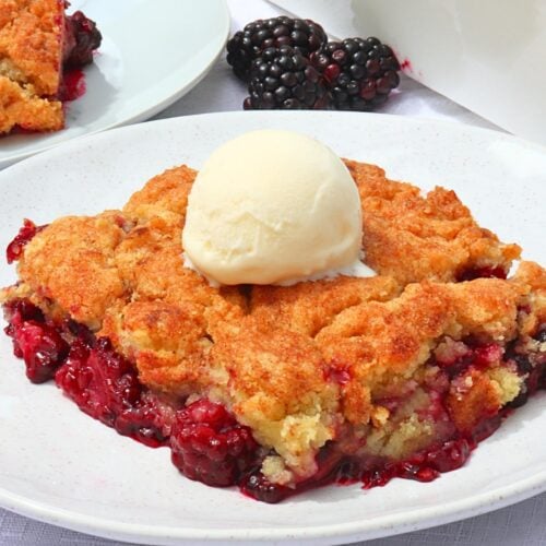 Slice of blackberry cobbler with a mound of vanilla ice cream on top, served on a white plate