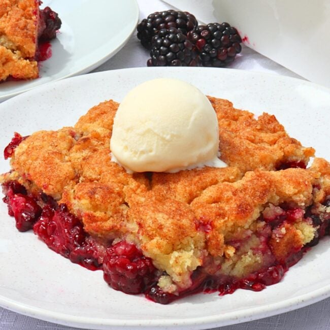 Slice of blackberry cobbler with a mound of vanilla ice cream on top, served on a white plate