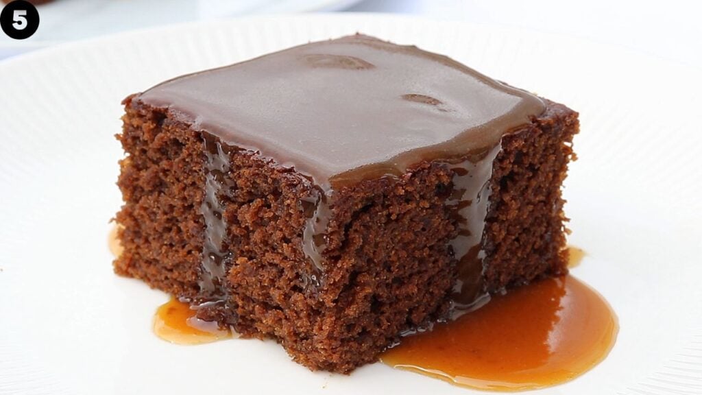 Square molasses cake with glossy butterscotch sauce on a white plate.