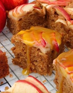Slices of apple spice cake with caramel drizzle and apple slices on top, close-up on a cooling rack