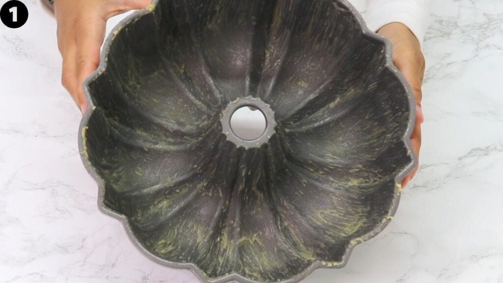 pumpkin bundt cake - Cakes by MK Top‑down view of a dark, fluted Bundt cake pan being held by two hands over a marble counter, center hole visible.