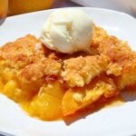 Warm peach cobbler with a scoop of vanilla ice cream on top, served on a white plate.