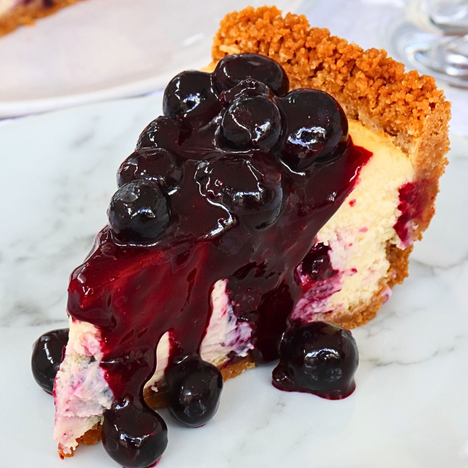 Slice of vanilla cake with a glossy blueberry cherry sauce dripping over it and a crumbly golden crust on the edge, served on a white plate