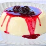 White frosted cake with red berry sauce dripping down the sides and topped with dark berries