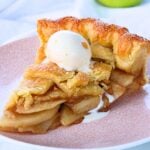 Slice of apple pie topped with a scoop of vanilla ice cream on a pink patterned plate.