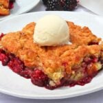 Slice of berry crumble pie on a white plate, topped with a scoop of vanilla ice cream.