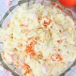 Creamy mixed potato and fruit salad topped with shredded coconut in a glass serving dish.