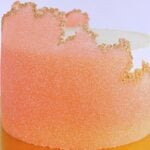 Close-up of a pink-orange frosted cake with a smooth, glittery surface and gold edible leaf along the top edge.