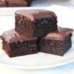 Two rich chocolate brownies stacked on a white plate, with glossy fudgy tops and dense crumb texture