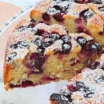 Sliced berry cake with blueberries and blackberries, dusted with powdered sugar on top.