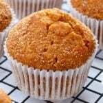 Golden-brown muffins with coarse sugar topping in white paper liners on a cooling rack