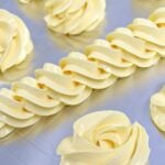 Pale-yellow buttercream swirls piped on a metal baking sheet, ready for decorating cookies or cakes.