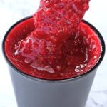 Close-up of bright red smoothie or sauce being poured into a black cup with a thick, glossy texture.