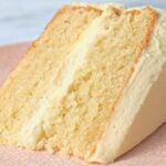 Slice of vanilla cake with white frosting on a pink patterned plate, close-up detail of the crumbly crumb.