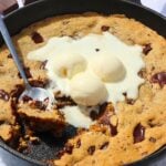Warm chocolate chip skillet cookie with vanilla ice cream scoops melting on top.