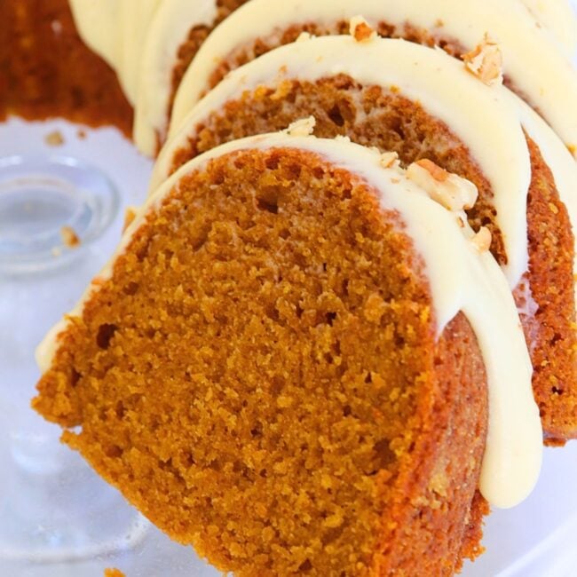 Slices of pumpkin cake with cream cheese frosting and almond pieces on top, arranged on a plate